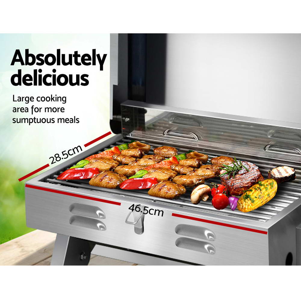 A portable stainless steel Grillz gas BBQ grill showing its grilling dimensions with steak, chicken wings, and vegetables cooking, grass in the background.