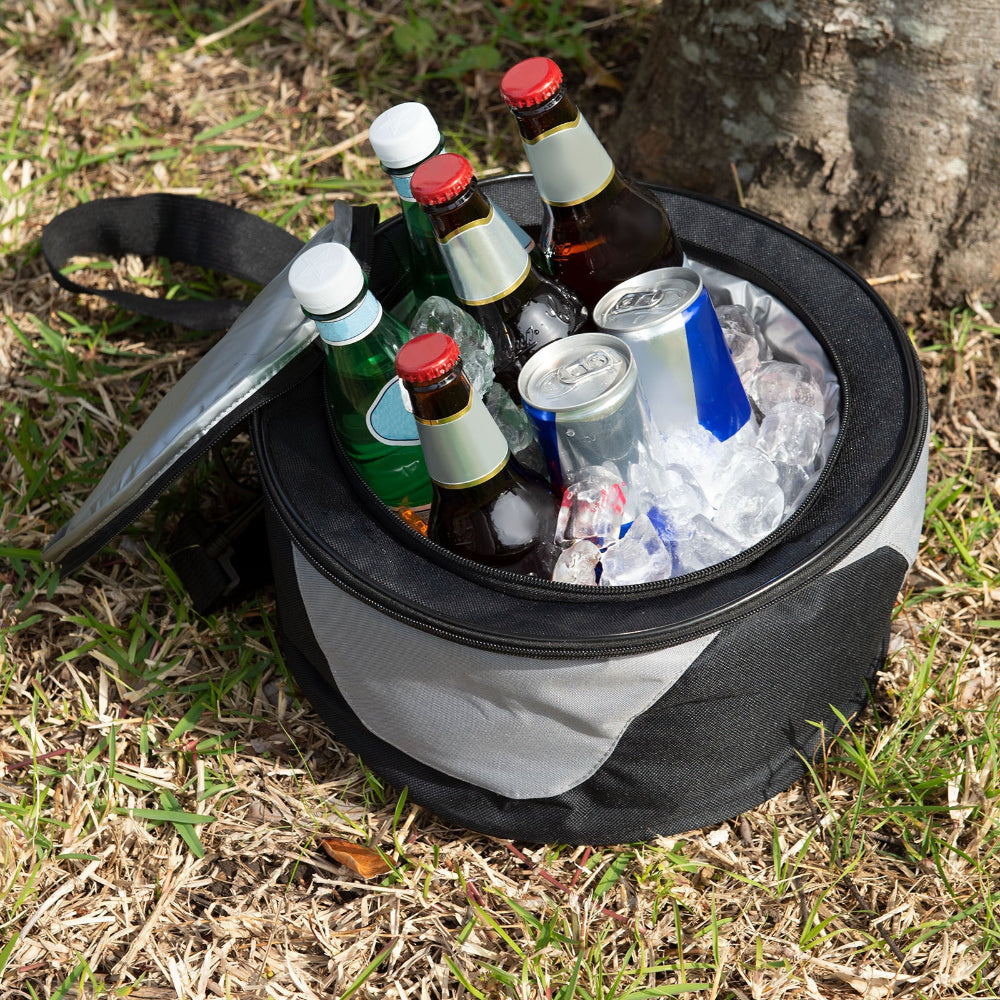 Portable cooler with drinks and ice set up on grass area beside a tree stump.