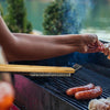 Person grilling sausages on a barbecue with a blurred natural background