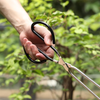 Person holding a pair of cooking tongs with a blurred green background