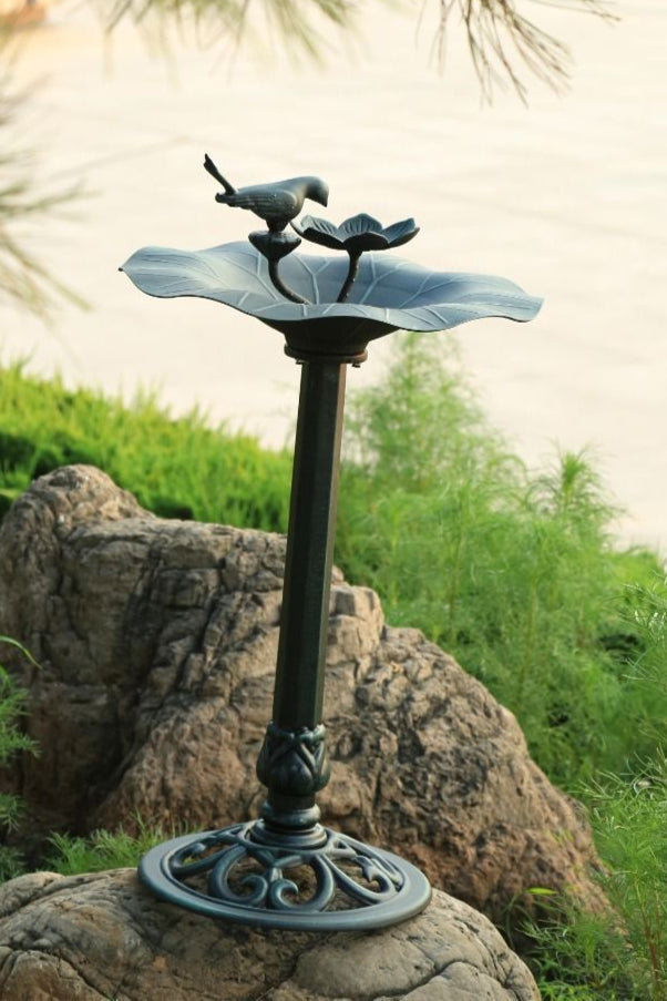 Decorative outdoor bird bath with two birds on a pedestal in a garden setting.