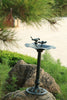 Decorative outdoor bird bath with two birds on a pedestal in a garden setting.