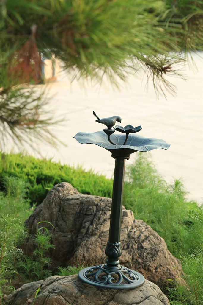 Decorative outdoor bird bath with two birds on a pedestal in a garden setting.