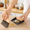 Person using a dustpan and brush set on a kitchen counter.