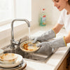 Person washing a dirty plate in a kitchen sink with gloves on