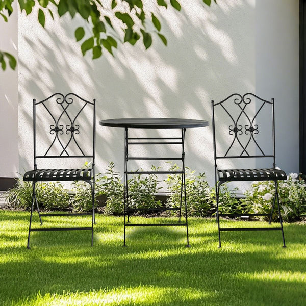 Black metal garden table and chairs on a grassy lawn with a white wall and greenery in the background.
