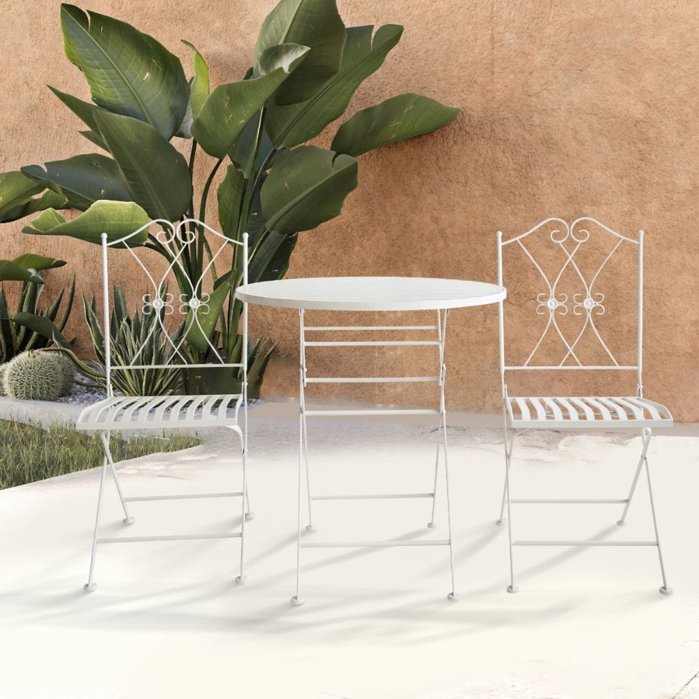 White metal outdoor table and chairs with decorative backrests on a light surface.