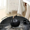 Black teapot and cup on a black wire bbq with white curtains in the background
