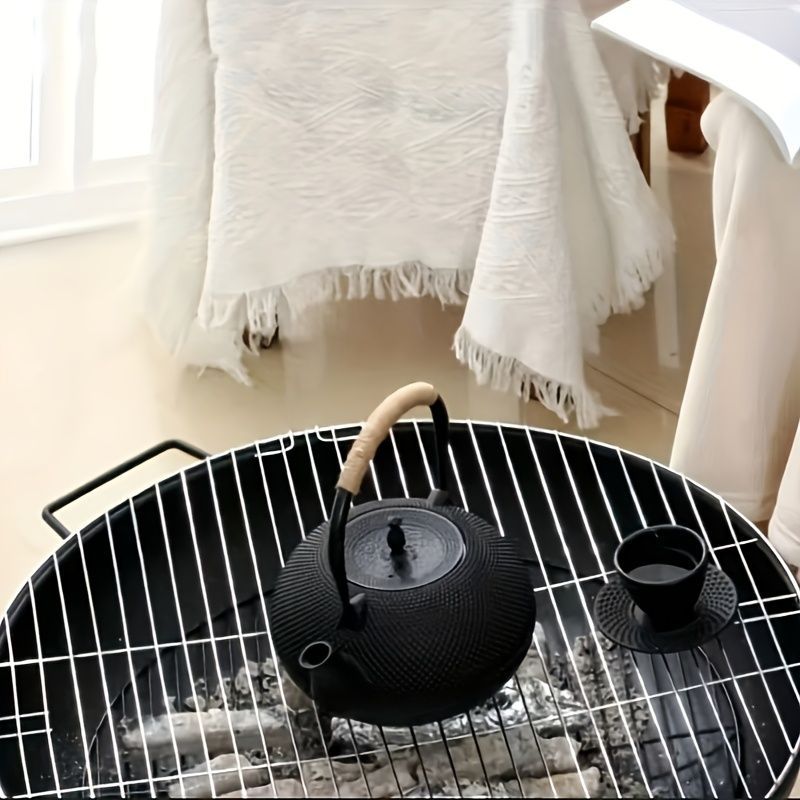 Black teapot and cup on a black wire bbq with white curtains in the background