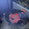 Small grill with glowing coals and a pot on top, placed on a tiled floor.