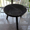 Black portable grill on a reflective surface with a blurred outdoor background