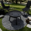 Black outdoor grill on a pebble circle with chairs and a table in a garden setting