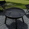 Black round grill on a pebbled surface with grass in the background