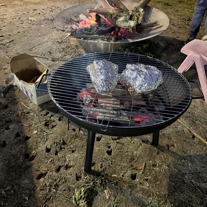 Barbecue grill with two pieces of meat on a dirt ground