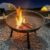 Fire pit with flames in a camping setting with tents and chairs in the background.