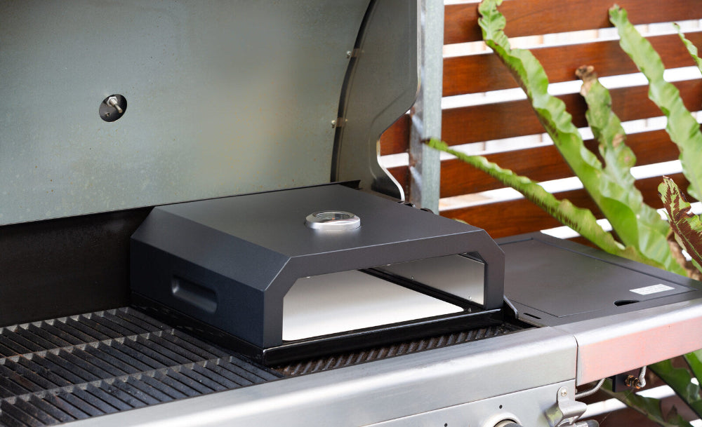 Portable pizza oven on a grill with plants in the background