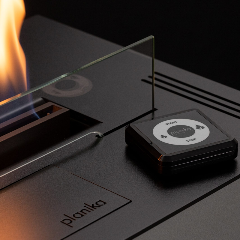 Planika stove with glass cover and flame, featuring the brand name.