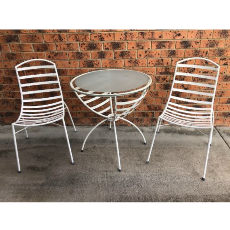 Two white metal chairs with a glass top table, set against a brick wall on an outdoor patio.