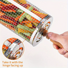 Hand holding a stainless-steel rotating grill basket with mix of vegetables inside it, and on a white background