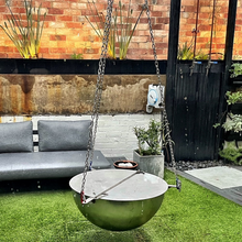 Load image into Gallery viewer, The Tripod Stainless Steel Fire Pit and stainless steel lid with poker hanging in an outdoor setting