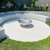 Cauldron round stainless-steel fire pit on cement tiled area with cement circular seating within a grassed area and plants in the background.