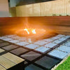 Cauldron round stainless-steel fire pit with a small fire burning. Fire pit is on cement tiles with small pebbles and a wooden seating area in a backyard setting.