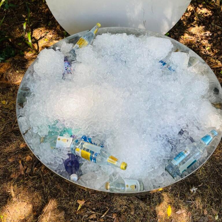 A polished mirror finished stainless steel fire pit filled with ice and bottles of drinks 