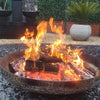 Cauldron round stainless-steel fire pit on gravel ground and a water feature and plants in a backyard setting.