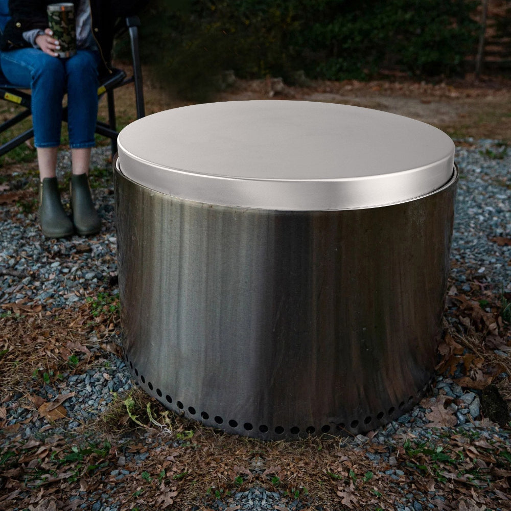 Metal fire pit with lid and a person sitting on a chair in the background