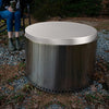 Metal fire pit with lid and a person sitting on a chair in the background
