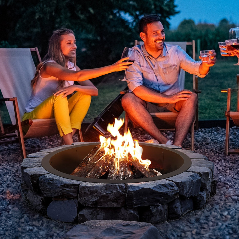 Two people sitting around a fire pit at night, enjoying drinks together.