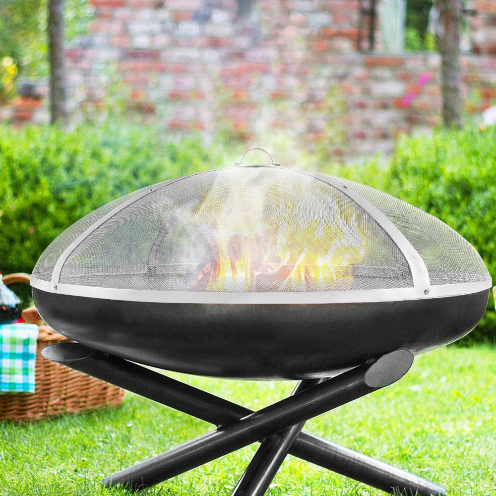 Portable fire pit with a mesh cover on a grassy area with a blurred background