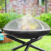 Portable fire pit with a mesh cover on a grassy area with a blurred background