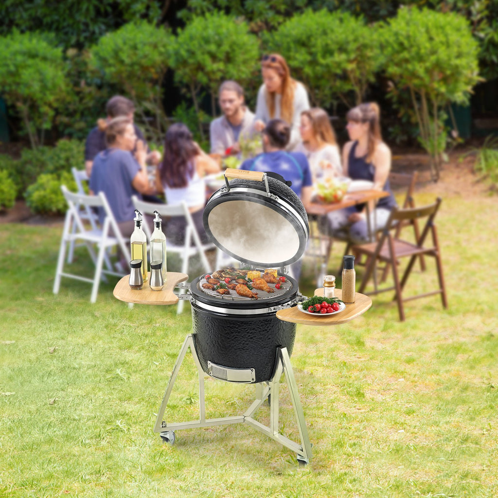 Outdoor grill with food on a grassy area with people sitting around a table in the background.