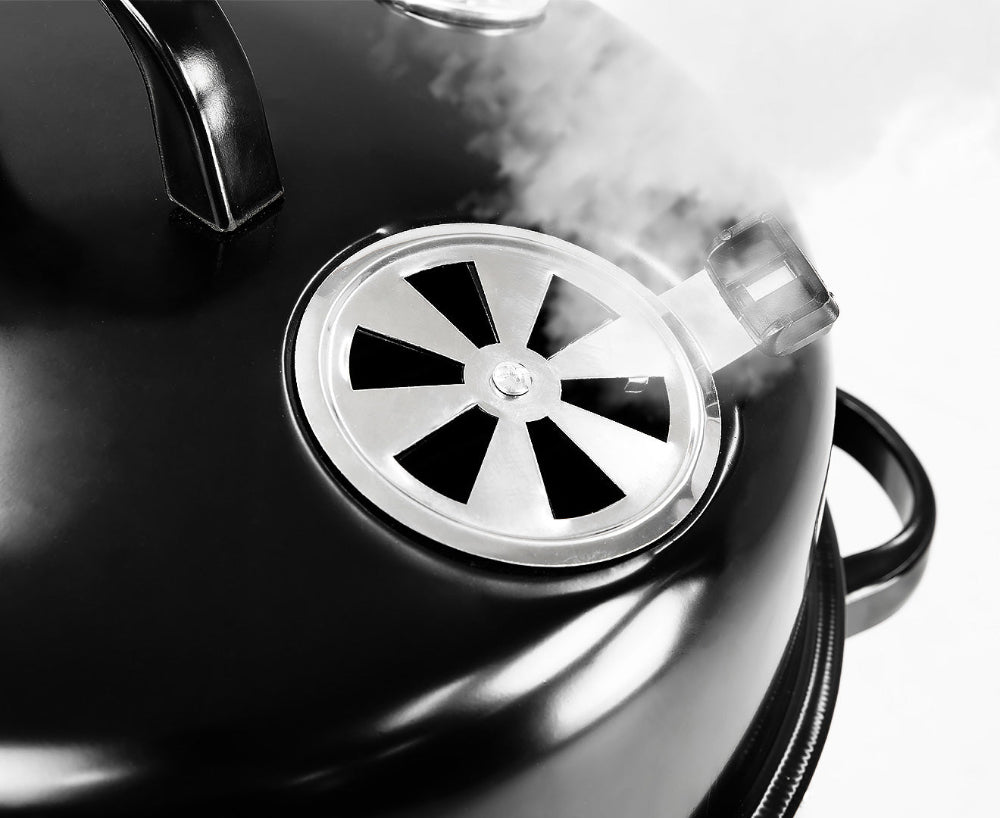 Black BBQ vent with a metallic lid and steam coming out it, set on a white background.