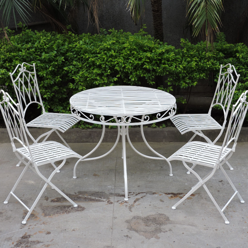 Albany 5-Piece Wrought Iron Setting in white on a cement floor area in front of green hedges and palm trees.