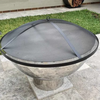 A circular metal ember screen on a round stainless steel fire pit, featuring in a private garden setting with cement paving and small lawn area.