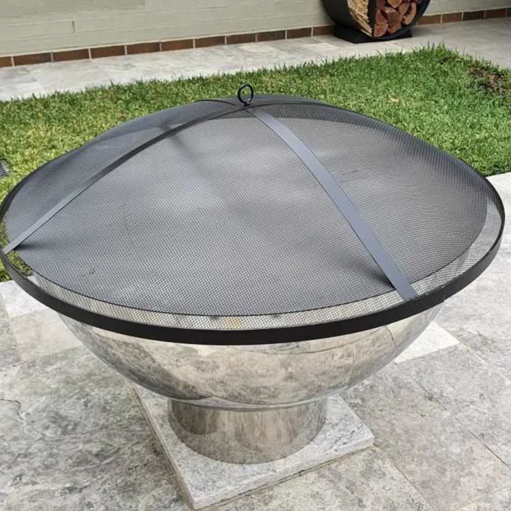 A circular metal ember screen on a round stainless steel fire pit, featuring in a private garden setting with cement paving and small lawn area.