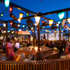 Galio Gas Fire Pit Insert Linear Automatic in an outdoor entertainment area, looks like a pub, lots of people sitting around, fans and flags set up on large pergola, wooden decking and seating all around the place.