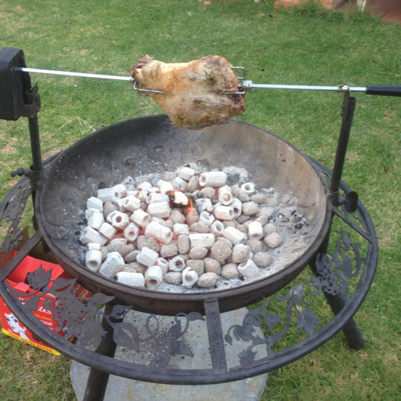 Spit Support Poles holding the Rotisserie and cooking a lamb roast on the Ultimate BBQ Fire Pit, on a lawn area.