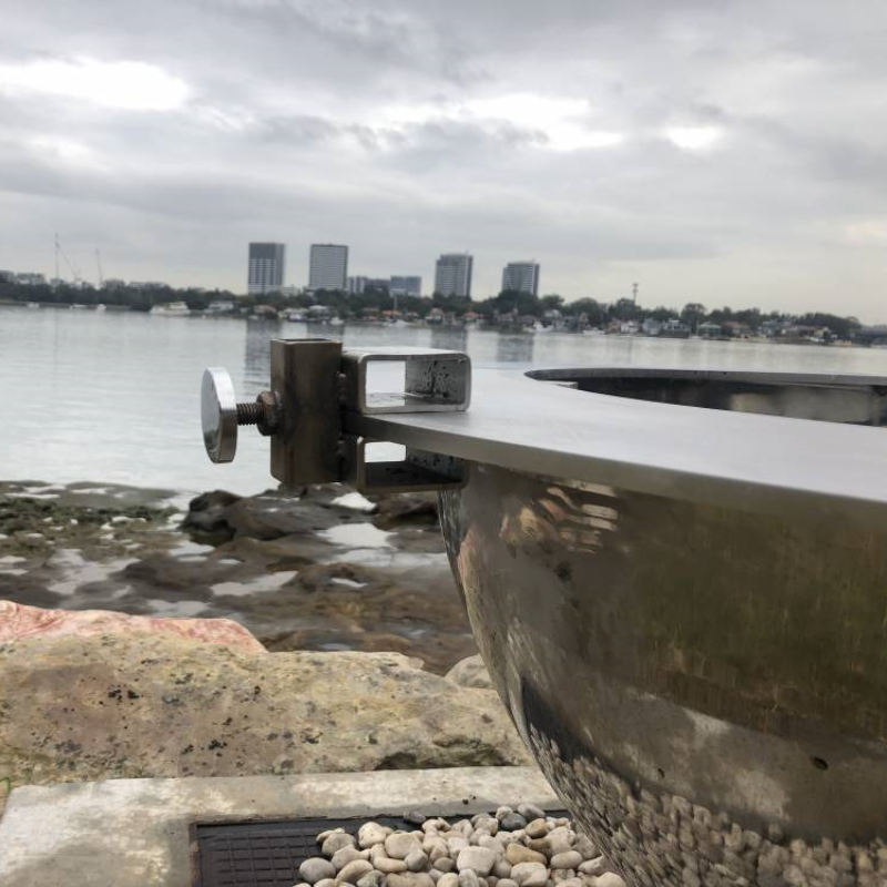 Teppanyaki Spit Rotisserie Bracket on side of the fire pit beside a body of water, buildings and boats in the background