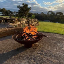 Load image into Gallery viewer, The Cauldron Fire Pit 1500mm burning a fire and half grill in background