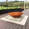 Rust-colored fire pit on a wooden deck with pebble and tiled surround, and scenic background of hills and trees