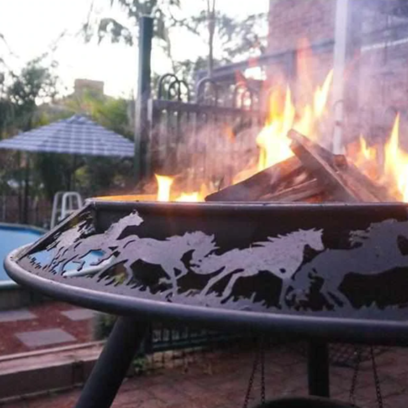 The Stockman designed Ultimate BBQ Fire Pit burning a fire on a brick paved area near poolside.