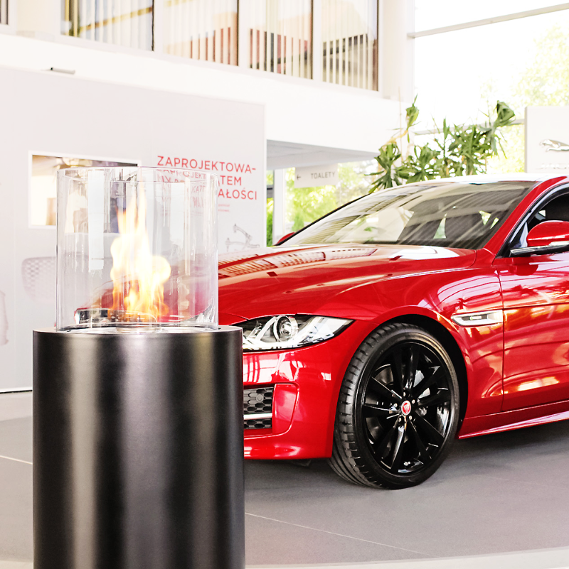 Totem Commerce Ethanol Burner in a commercial car showroom in Poland, set beside a red car and office behind them.
